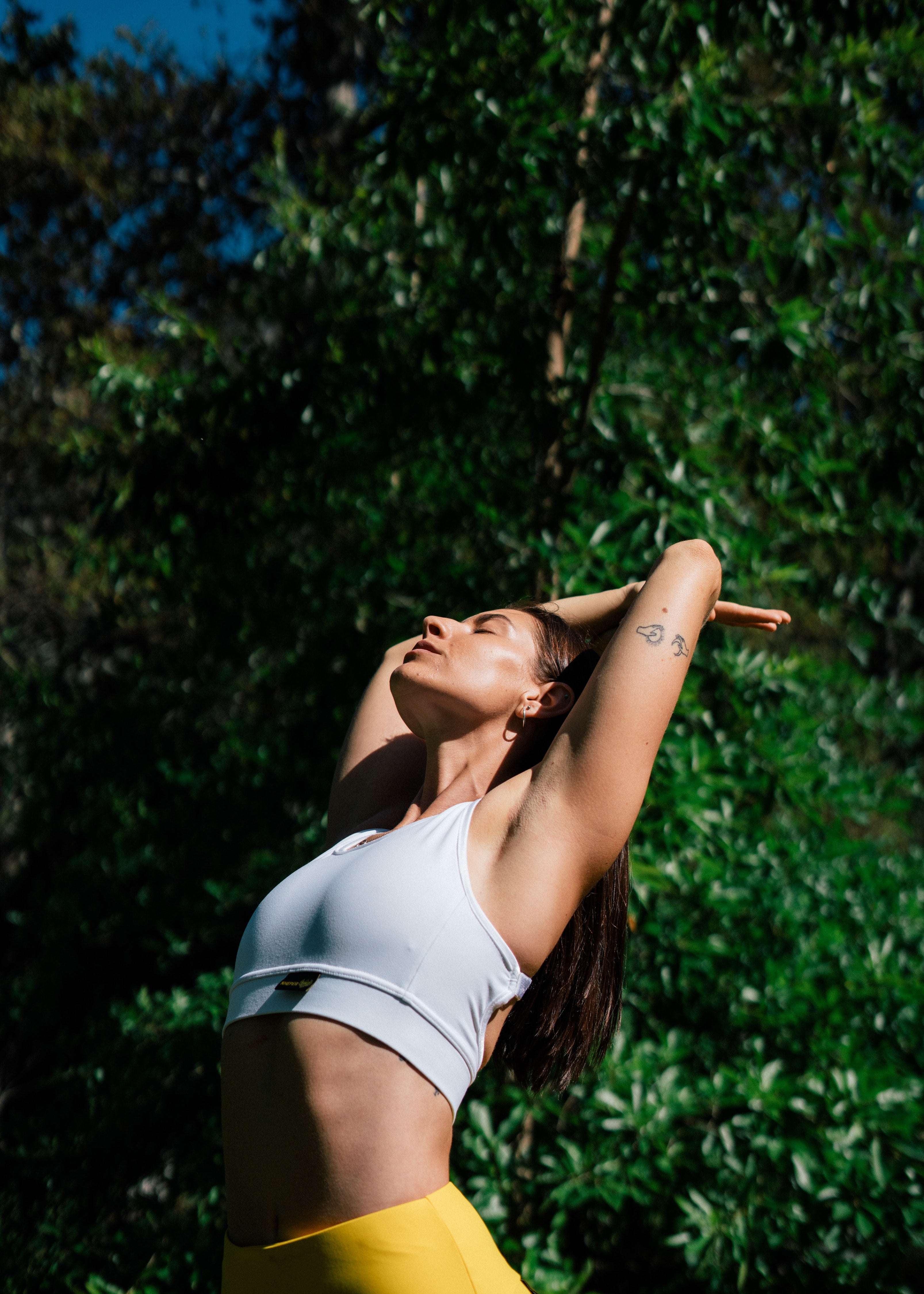Woman stretching outdoors in front of a tall shrub