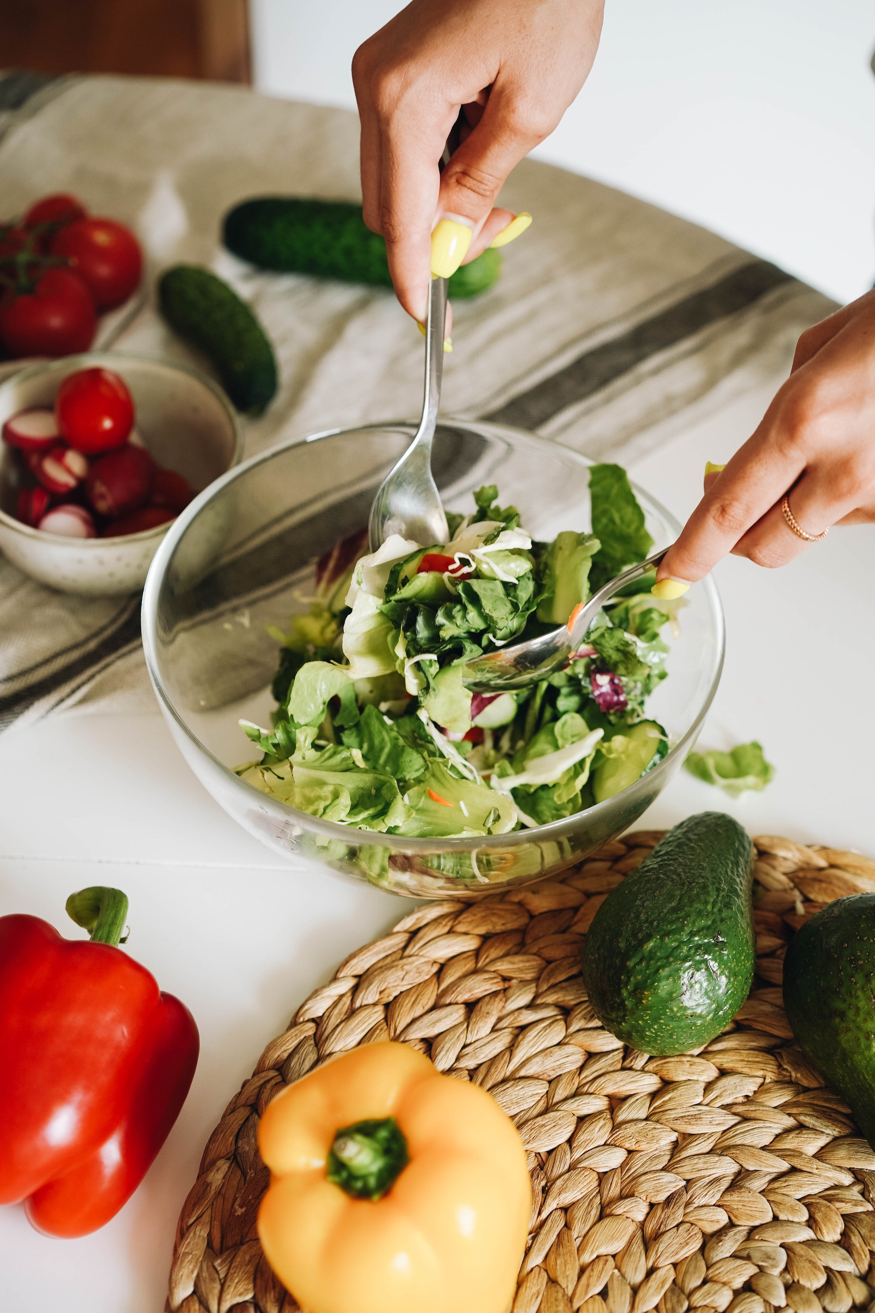 Person making a salad with avocado, radishes, cucumbers, red peppers, and lettuce.