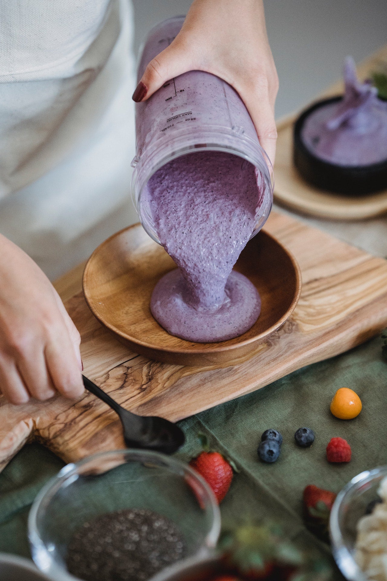 Person pouring blueberry smoothie into wooden bowl