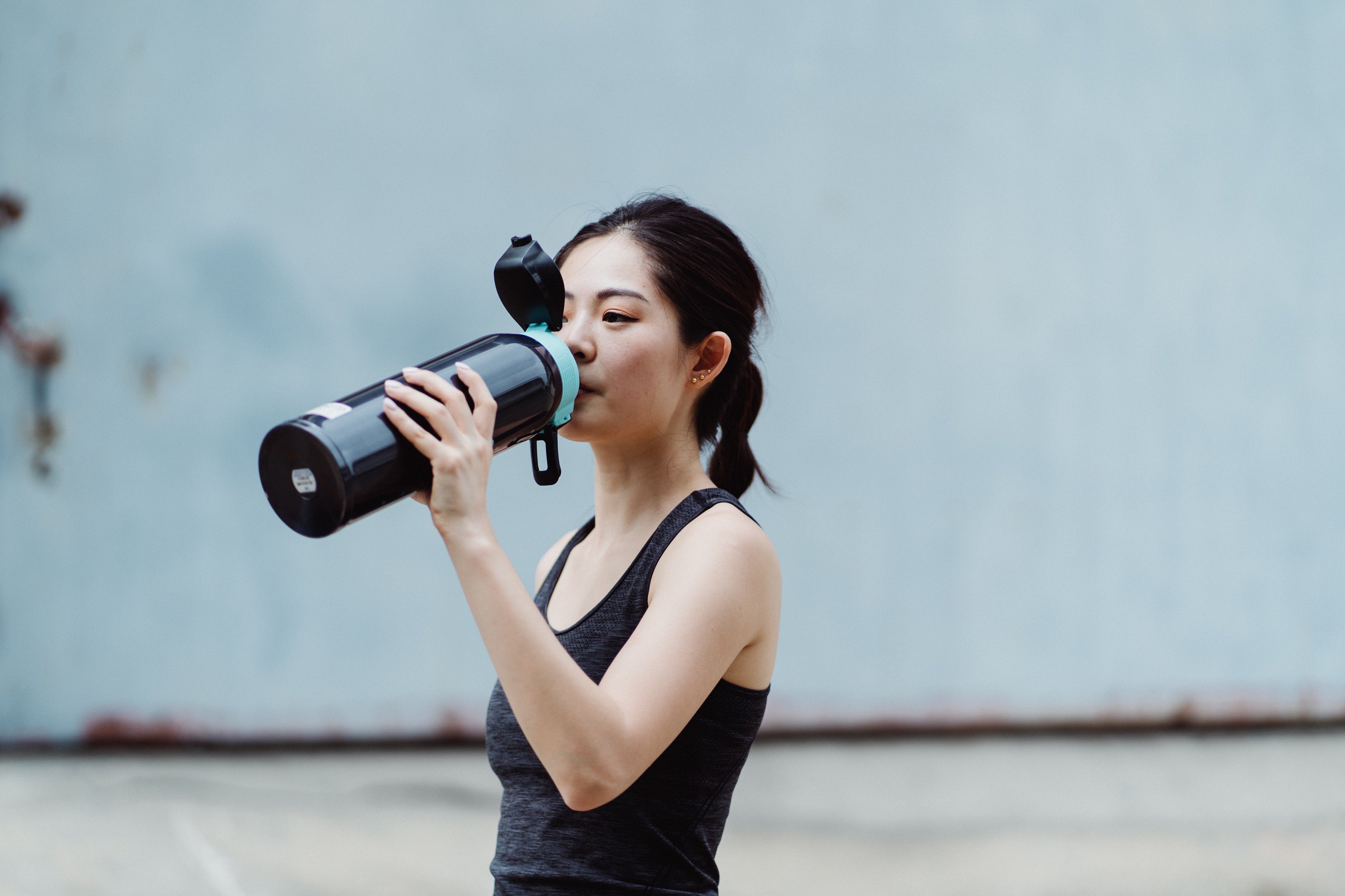 A woman in atheltic wear drinking out of a reusable water bottle