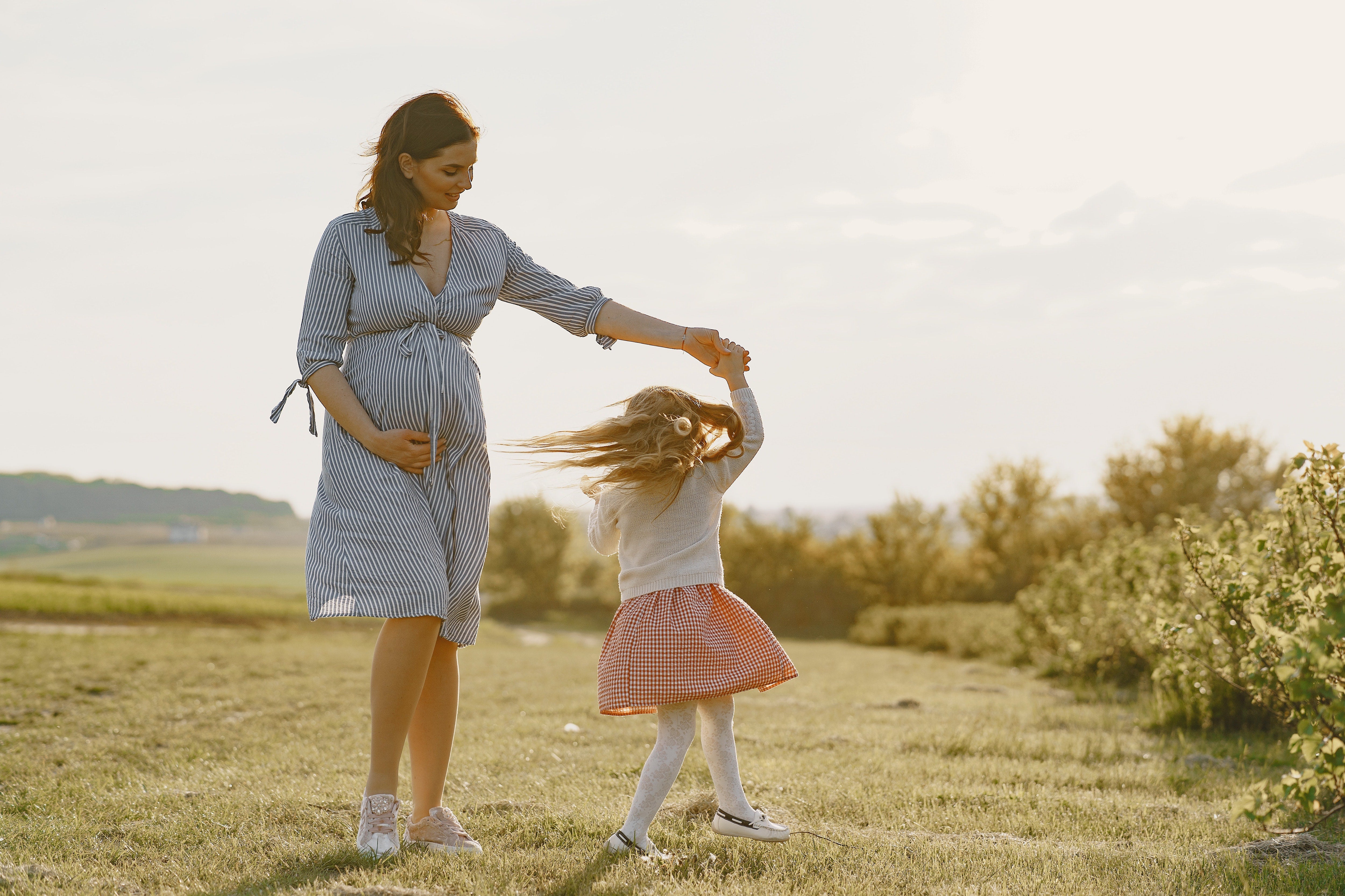 Pregnant mother twirling her daughter in a field of grass