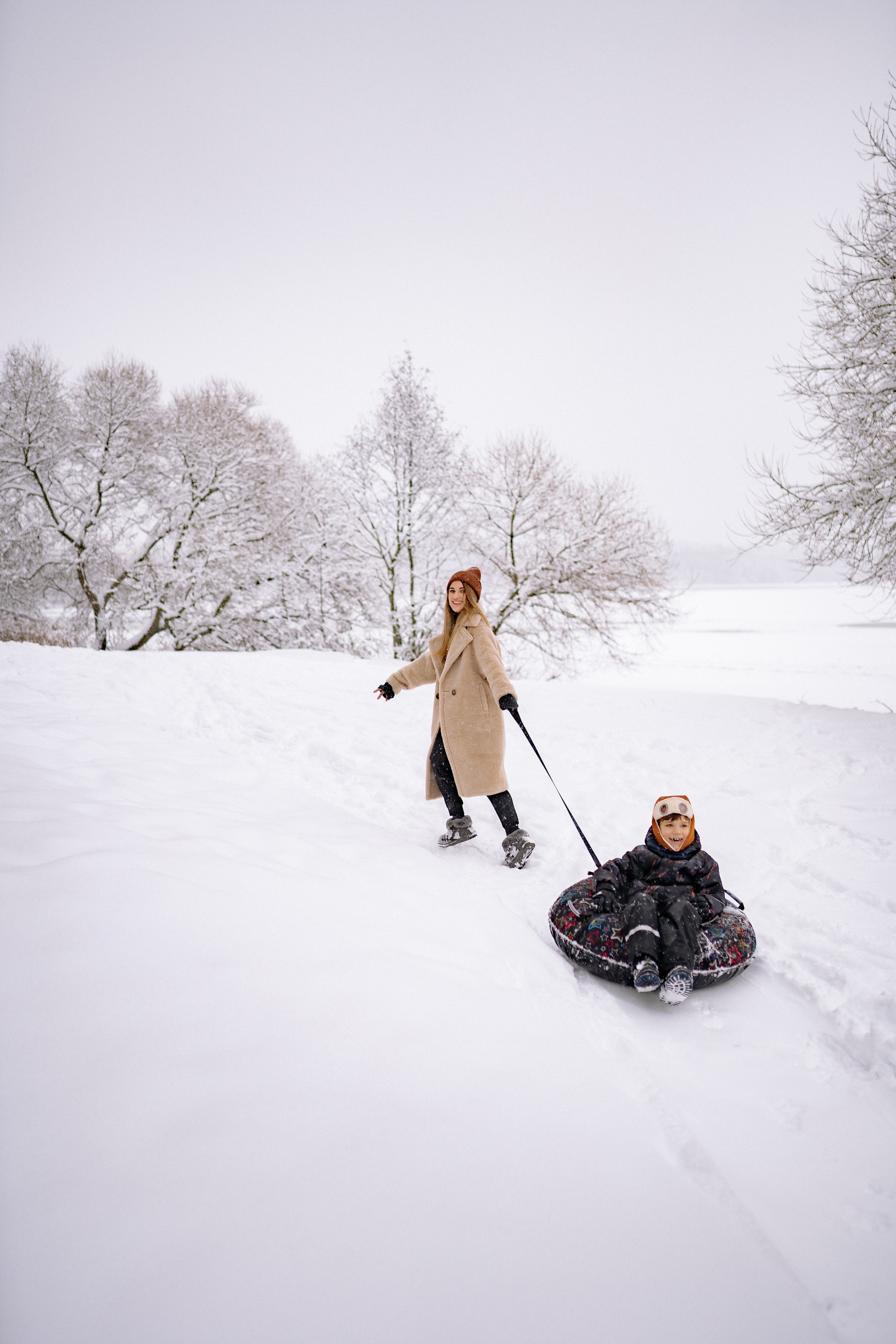 A mother pulling her child in a tubing slope through the snow 