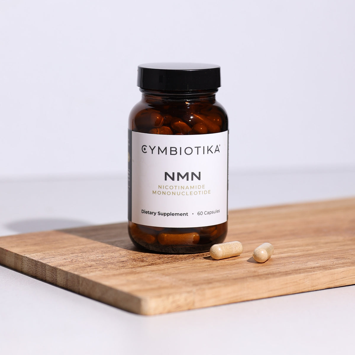 NMN + Trans-Resveratrol bottle sitting on a cutting-board, next to 2 NMN + Trans-Resveratrol capsules